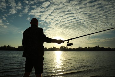 Photo of Fisherman with rod fishing at riverside at sunset, back view