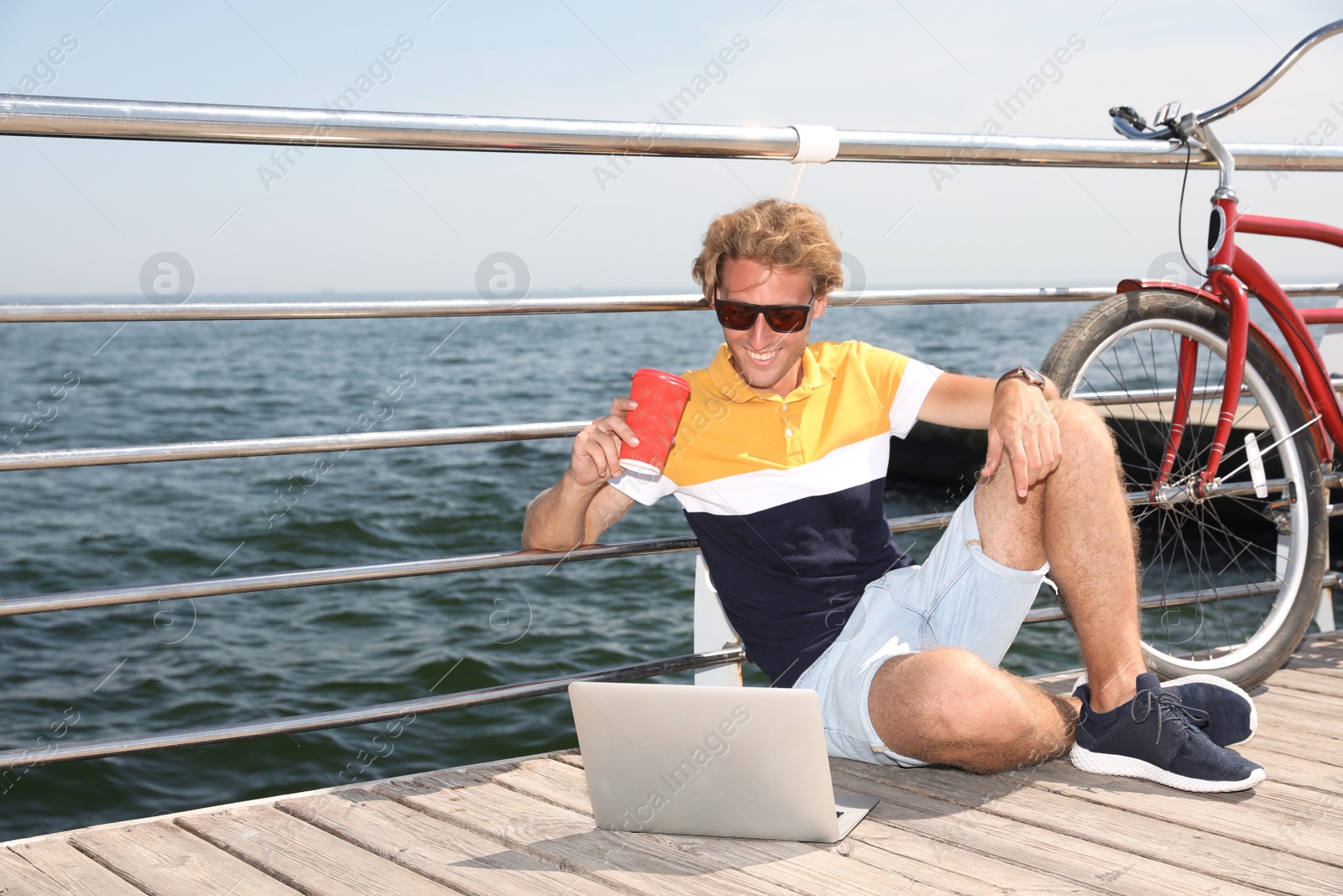 Photo of Attractive man with laptop and bike near sea on sunny day, space for text