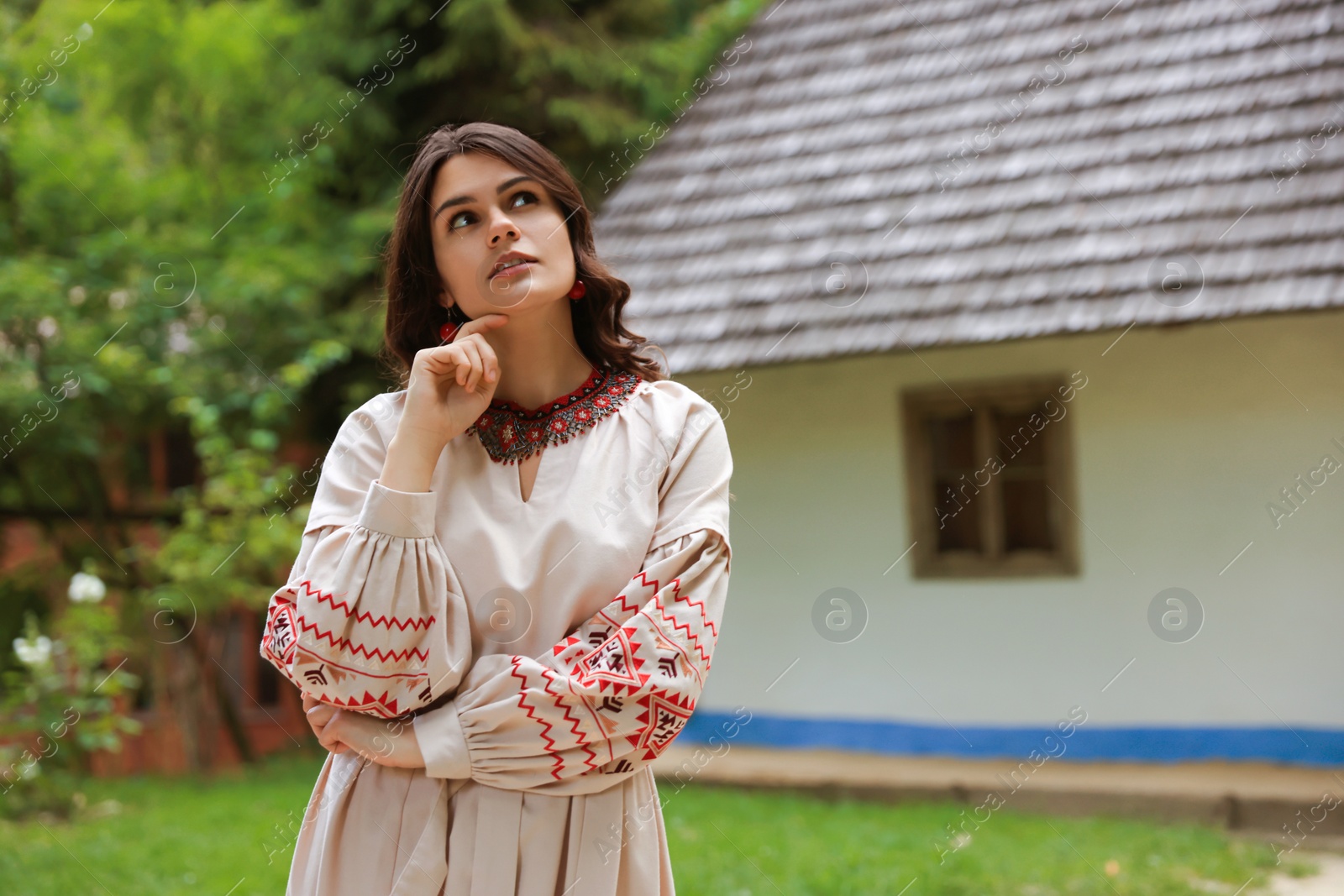 Photo of Beautiful woman wearing embroidered dress in village, space for text. Ukrainian national clothes