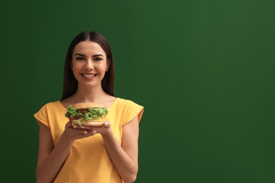 Photo of Young woman with tasty burger on color background. Space for text