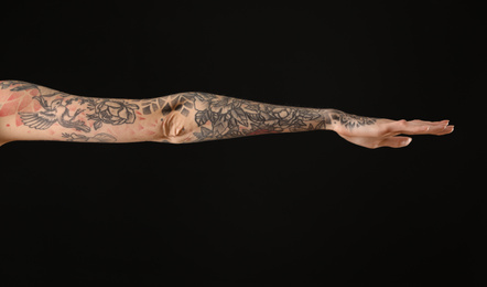 Woman with colorful tattoos on arm against black background, closeup