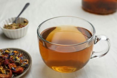 Photo of Cup of freshly brewed tea, dried herbs and berries on white table