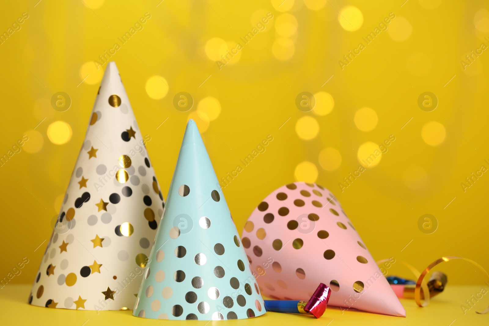 Photo of Party hats and festive items on table against yellow background with blurred lights. Space for text