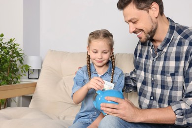 Photo of Little girl with her father putting money into piggy bank at home
