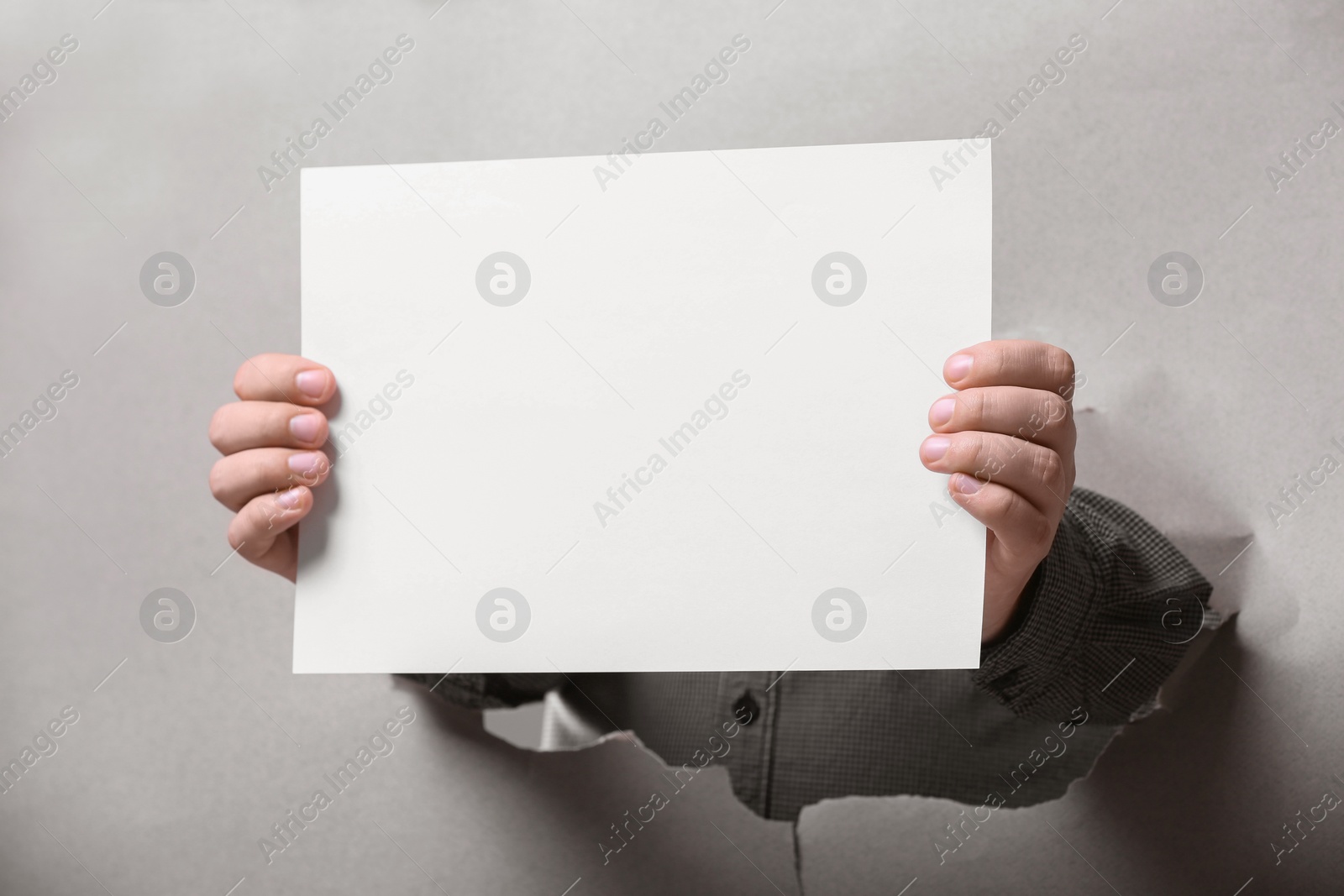 Photo of Man holding sheet of paper through hole in white paper, closeup. Mockup for design