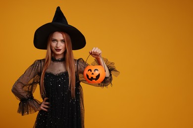 Young woman in scary witch costume with pumpkin bucket on orange background, space for text. Halloween celebration