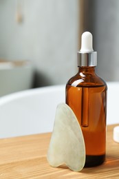 Photo of Jade gua sha tool and cosmetic product on wooden caddy in bathroom