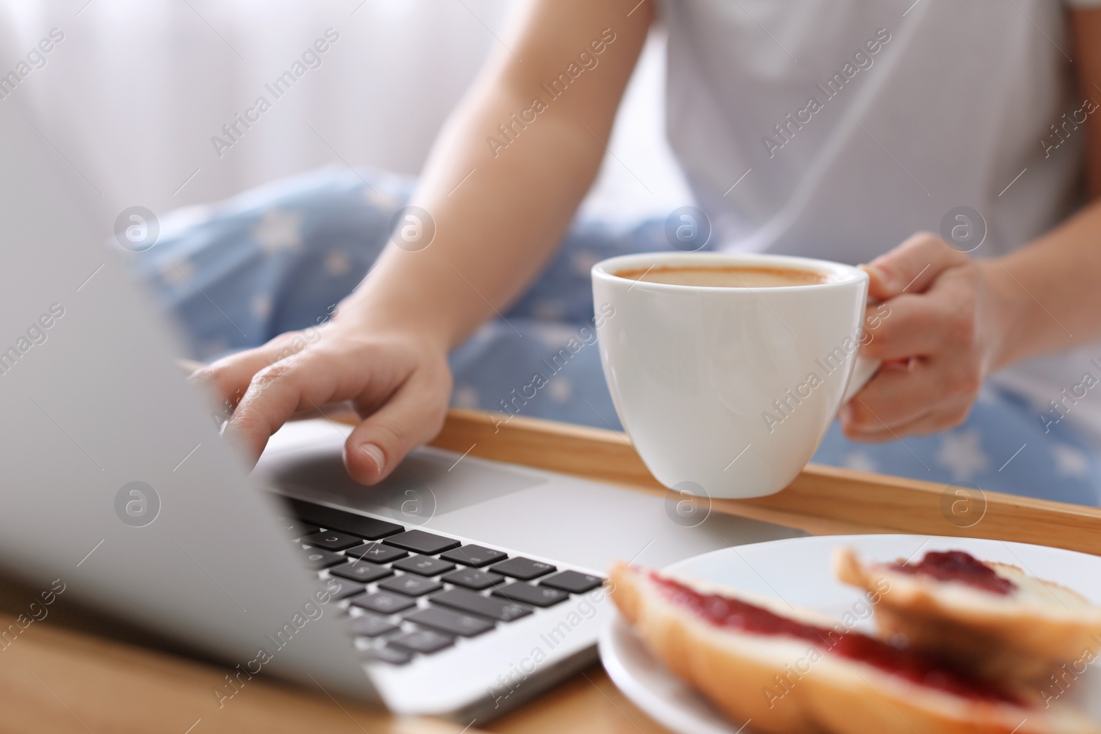 Photo of Woman with cup of morning coffee working on laptop indoors, closeup