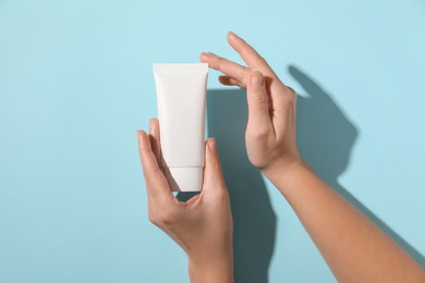 Woman with tube of hand cream on light blue background, top view