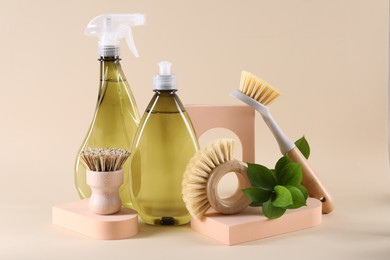 Photo of Bottles of cleaning product, brushes and floral decor on beige background