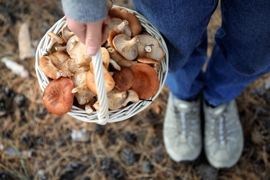 Photo of Woman holding wicker basket with fresh wild mushrooms in forest, above view