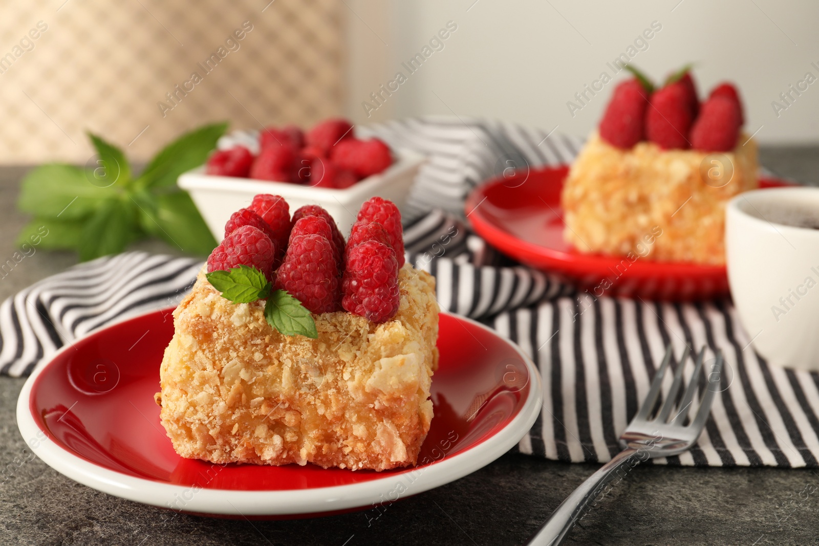 Photo of Piece of delicious Napoleon cake with fresh raspberries served on grey table, closeup. Space for text