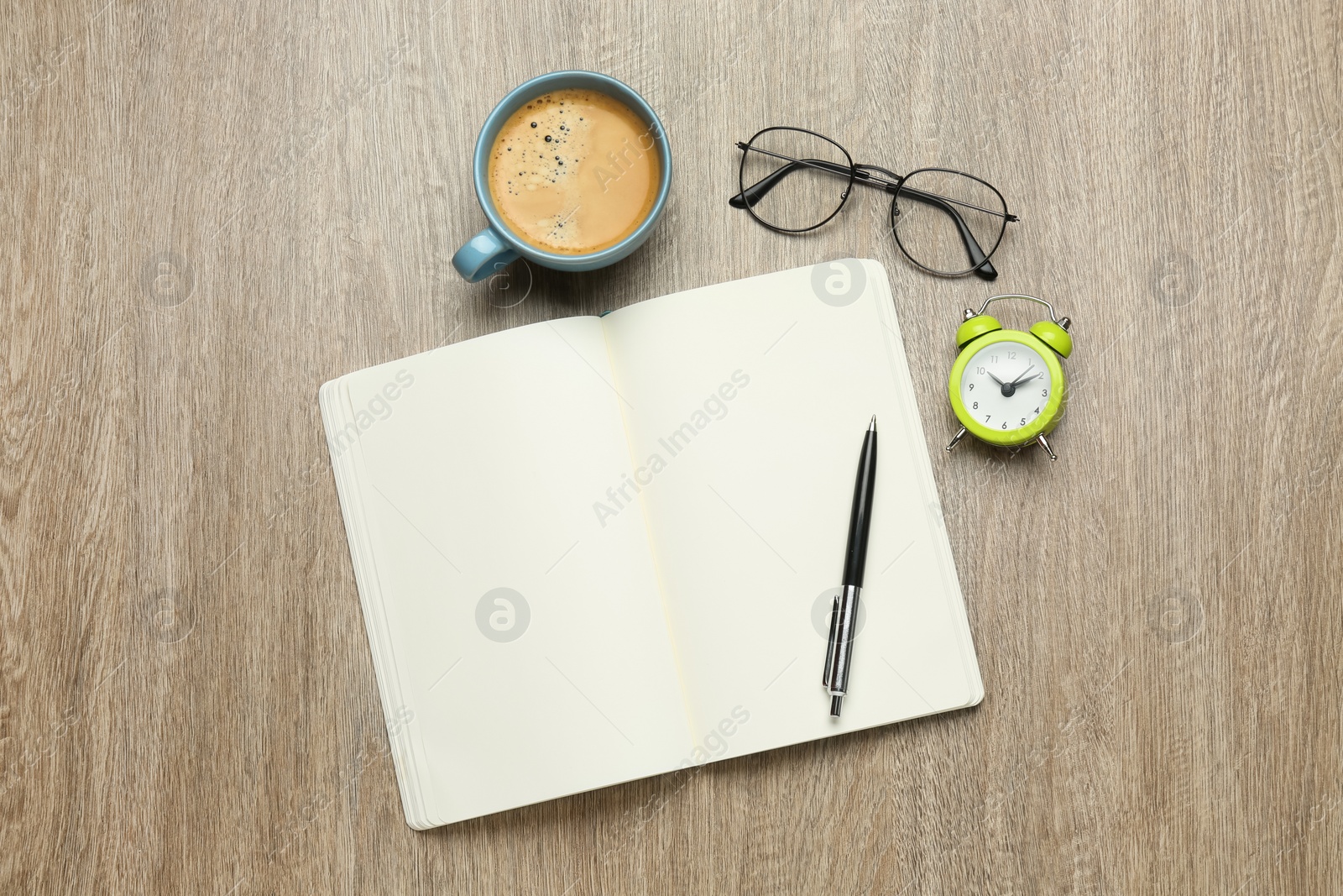 Photo of Open notebook, glasses, alarm clock, pen and cup of coffee on wooden table, flat lay