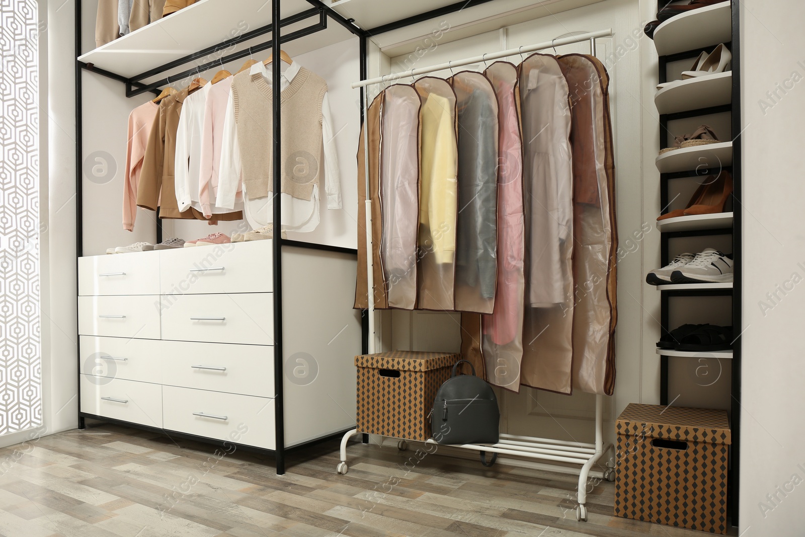 Photo of Garment bags with clothes on rack in dressing room