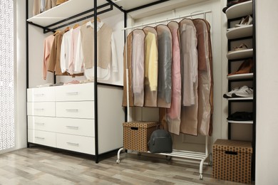 Photo of Garment bags with clothes on rack in dressing room