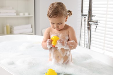 Photo of Cute little girl with rubber ducks in foamy bath at home
