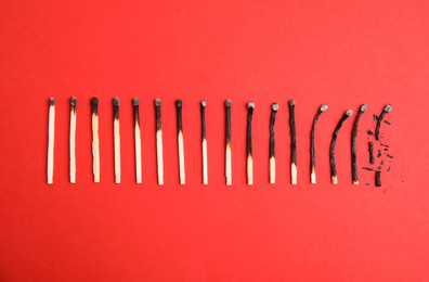 Photo of Different stages of burnt matches on red background, flat lay