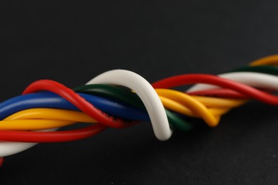 Photo of Many twisted electrical cables on black background, closeup