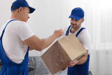 Photo of Workers wrapping box in stretch film indoors