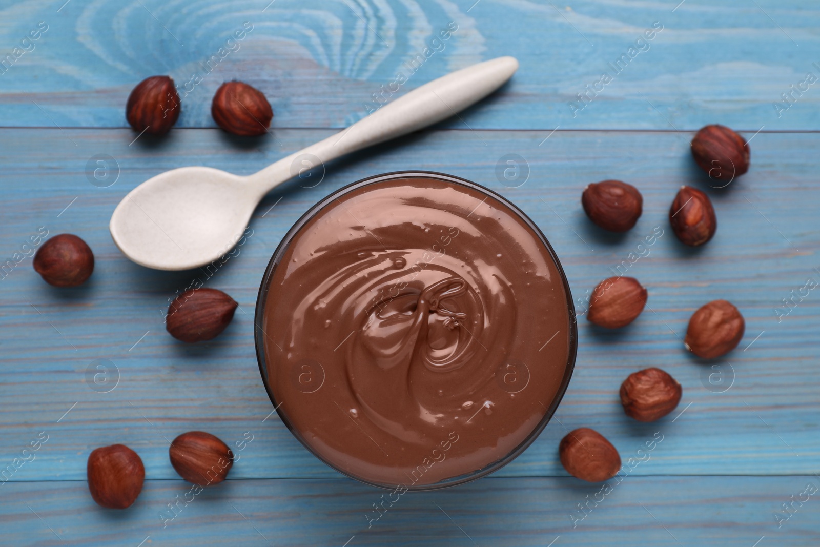 Photo of Bowl with tasty chocolate paste and nuts on light blue wooden table, flat lay