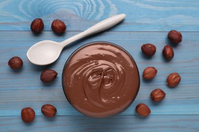 Bowl with tasty chocolate paste and nuts on light blue wooden table, flat lay
