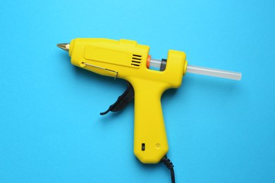 Photo of Yellow glue gun with stick on light blue background, top view