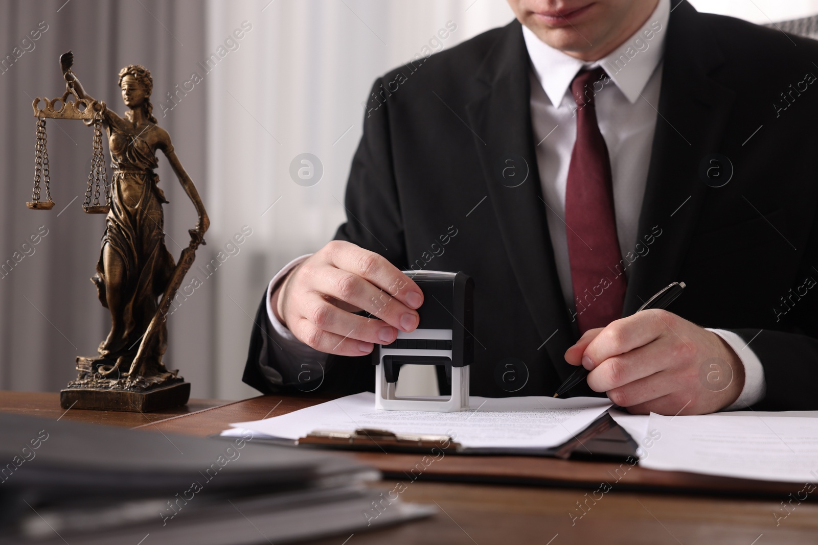 Photo of Notary with pen stamping document at wooden table in office, closeup