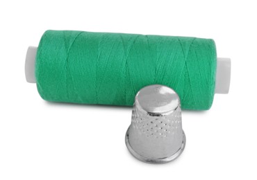 Photo of Thimble and spool of green sewing thread isolated on white