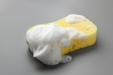 Photo of Yellow sponge with foam on grey background, closeup