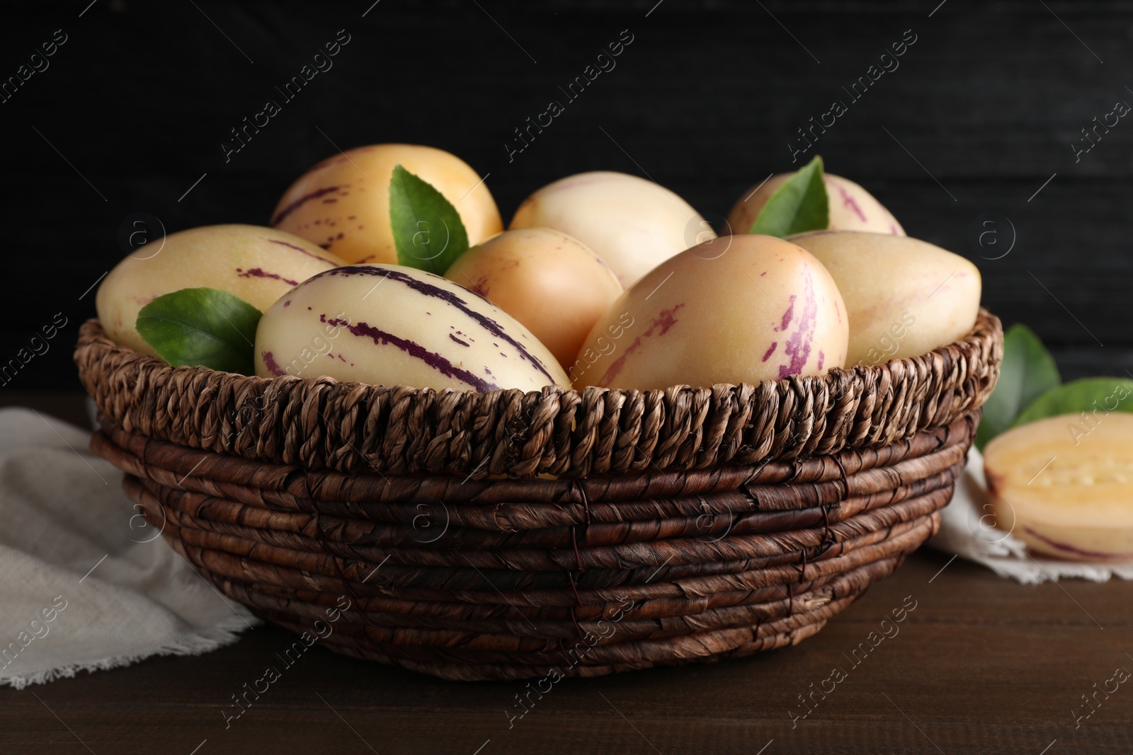 Photo of Fresh ripe pepino melons with green leaves in wicker basket on wooden table