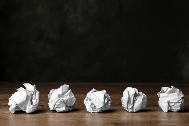Photo of Balls of crumpled paper on wooden table against dark background, space for text