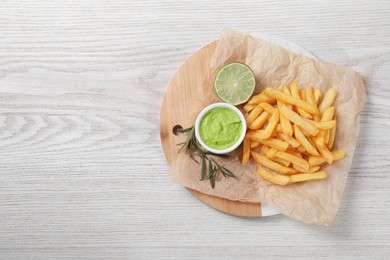 Photo of Delicious french fries, avocado dip, lime and rosemary served on white wooden table, top view. Space for text