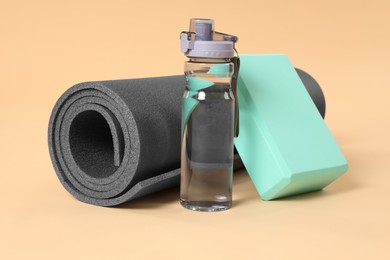 Photo of Grey exercise mat, yoga block and bottle of water on beige background