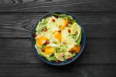 Photo of Delicious salad with Chinese cabbage, lemon, persimmon and pomegranate seeds on black wooden table, top view