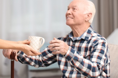 Elderly man taking cup of tea from female caregiver at home