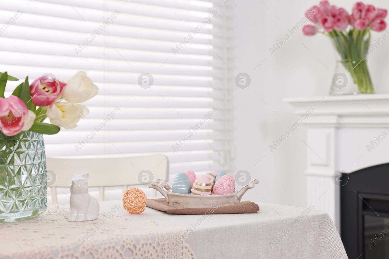 Photo of Easter decorations. Bouquet of tulips in vase, painted eggs and bunny figure on white table at home