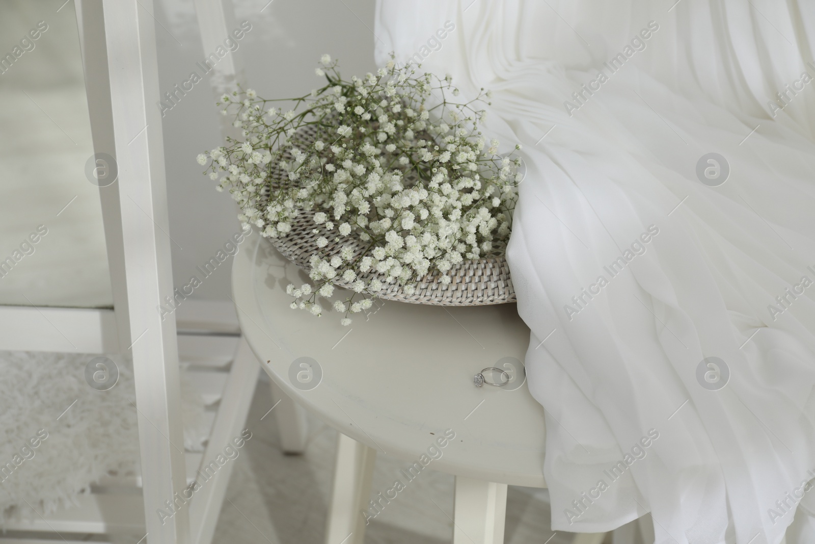 Photo of Beautiful engagement ring, flowers and wedding dress on table indoors, closeup