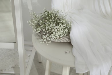 Photo of Beautiful engagement ring, flowers and wedding dress on table indoors, closeup