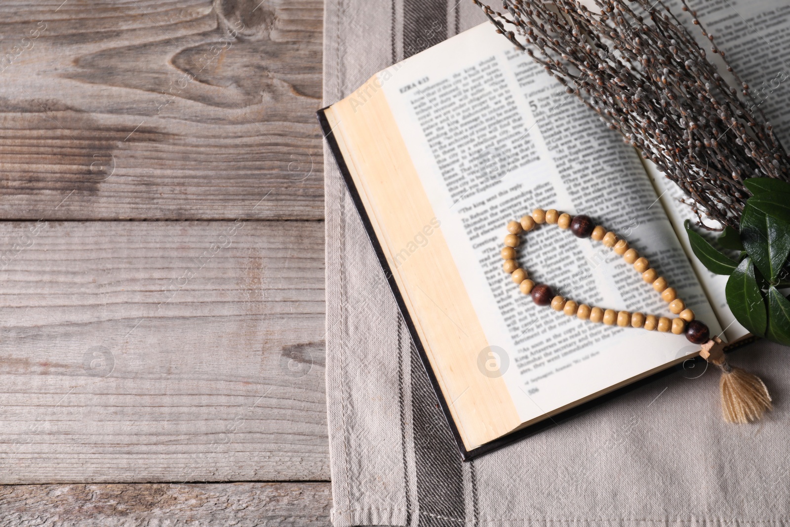Photo of Rosary beads, Bible and willow branches on wooden table, flat lay. Space for text