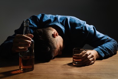 Photo of Addicted man with alcoholic drink at wooden table indoors, focus on hands
