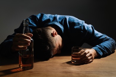 Addicted man with alcoholic drink at wooden table indoors, focus on hands