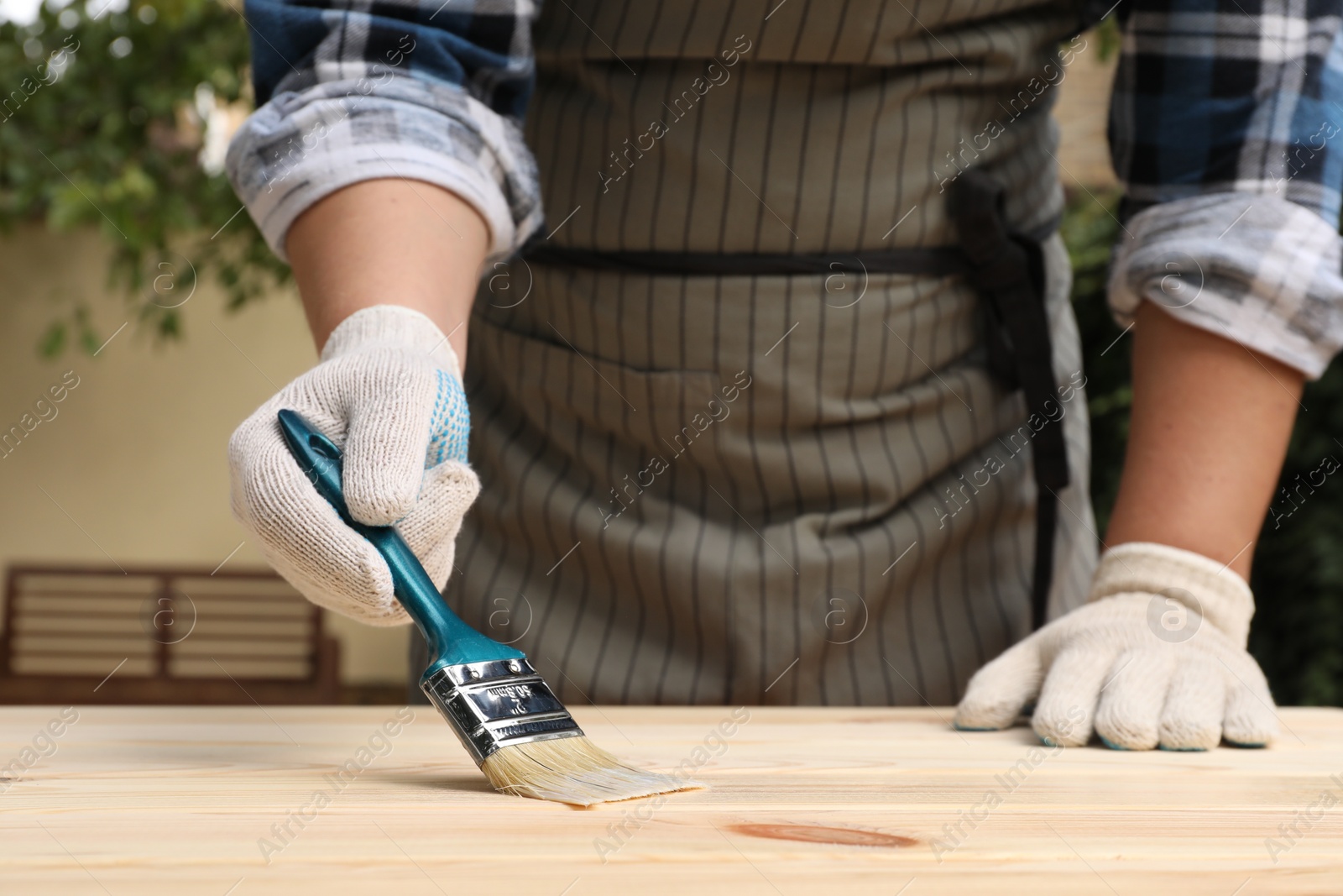 Photo of Man varnishing wooden surface with brush outdoors, closeup