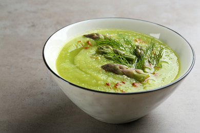 Photo of Delicious asparagus soup in bowl on grey table