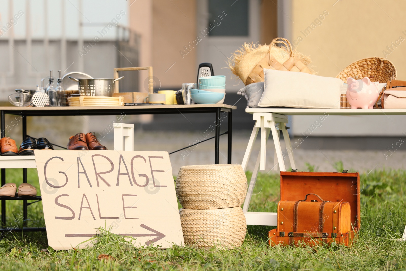 Photo of Sign Garage sale written on cardboard near tables with different stuff in yard