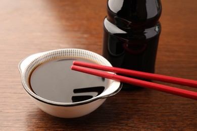 Bottle, bowl with soy sauce and chopsticks on wooden table, closeup