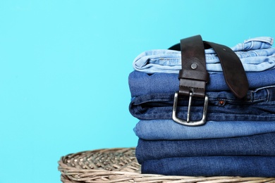 Photo of Stack of different jeans on basket against color wall with space for text