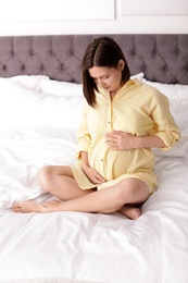 Photo of Beautiful pregnant woman sitting on bed at home