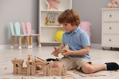 Photo of Little boy playing with wooden construction set on floor in room. Child's toy