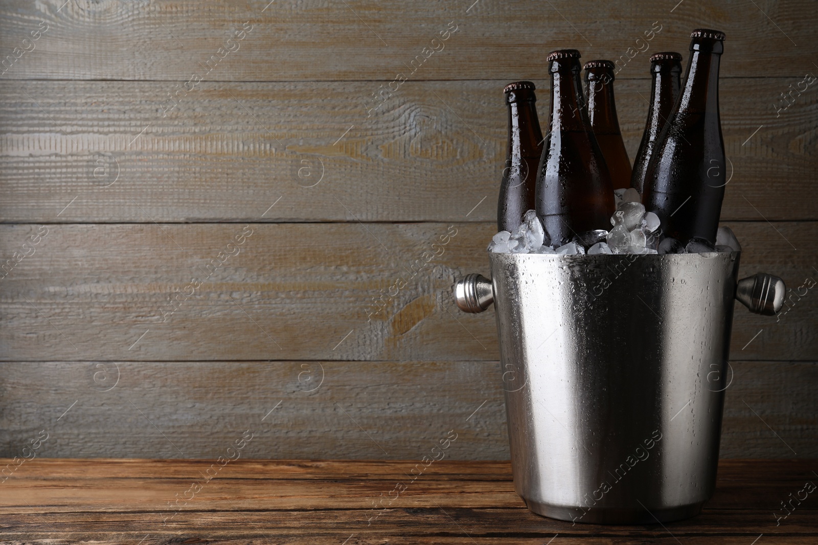 Photo of Metal bucket with beer and ice cubes on wooden table. Space for text