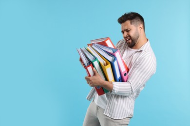 Photo of Stressful man with folders on light blue background, space for text